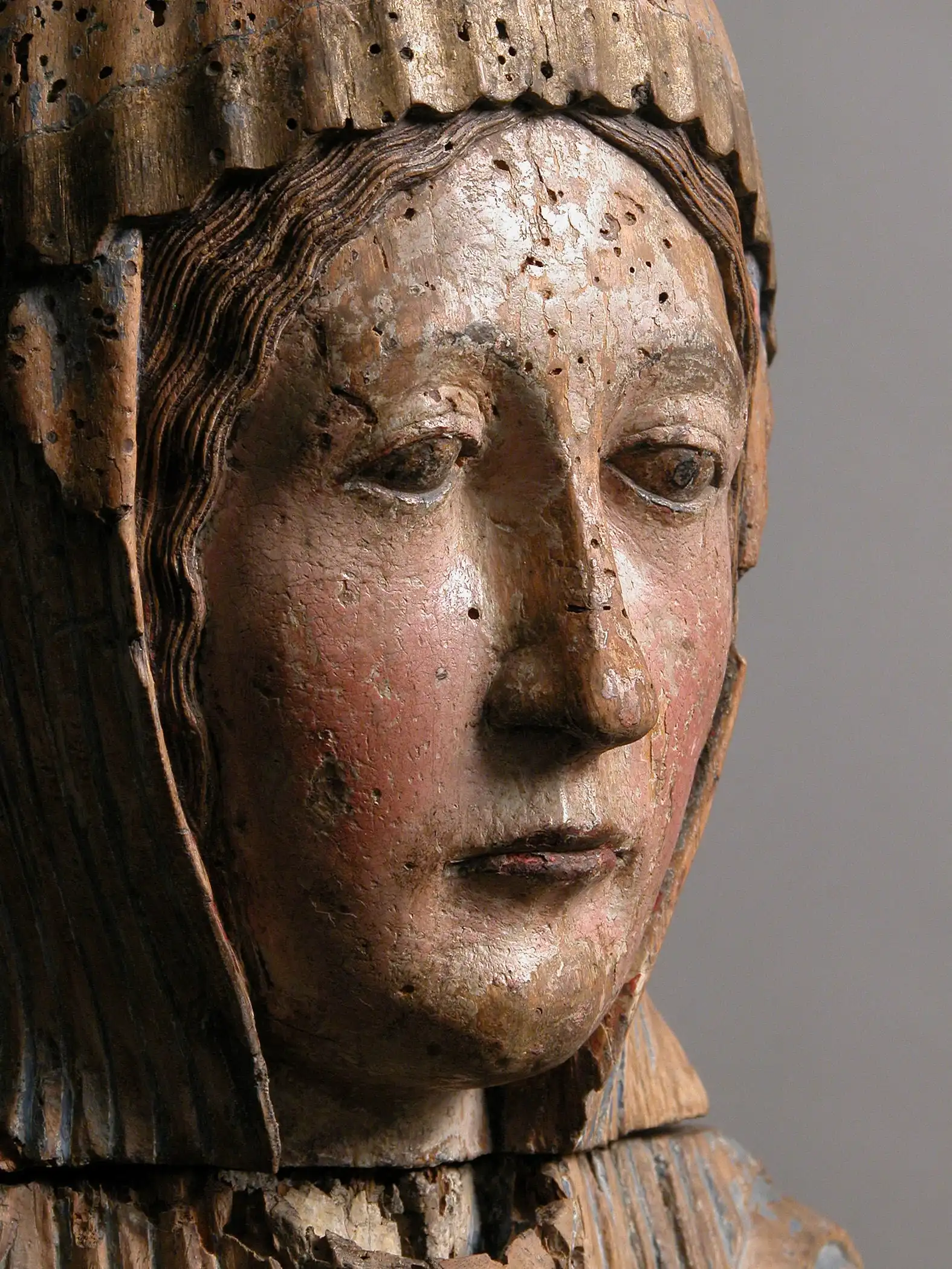The image shows a close-up of the Virgin Mary’s face, carved in wood and originally polychromed, with visible wear from age and devotion.