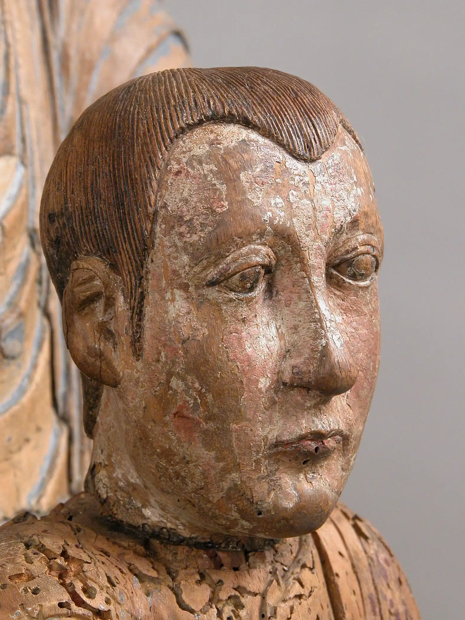 The image shows a close-up of the Christ Child’s face, carved in wood and once richly polychromed, now marked by wear and age.