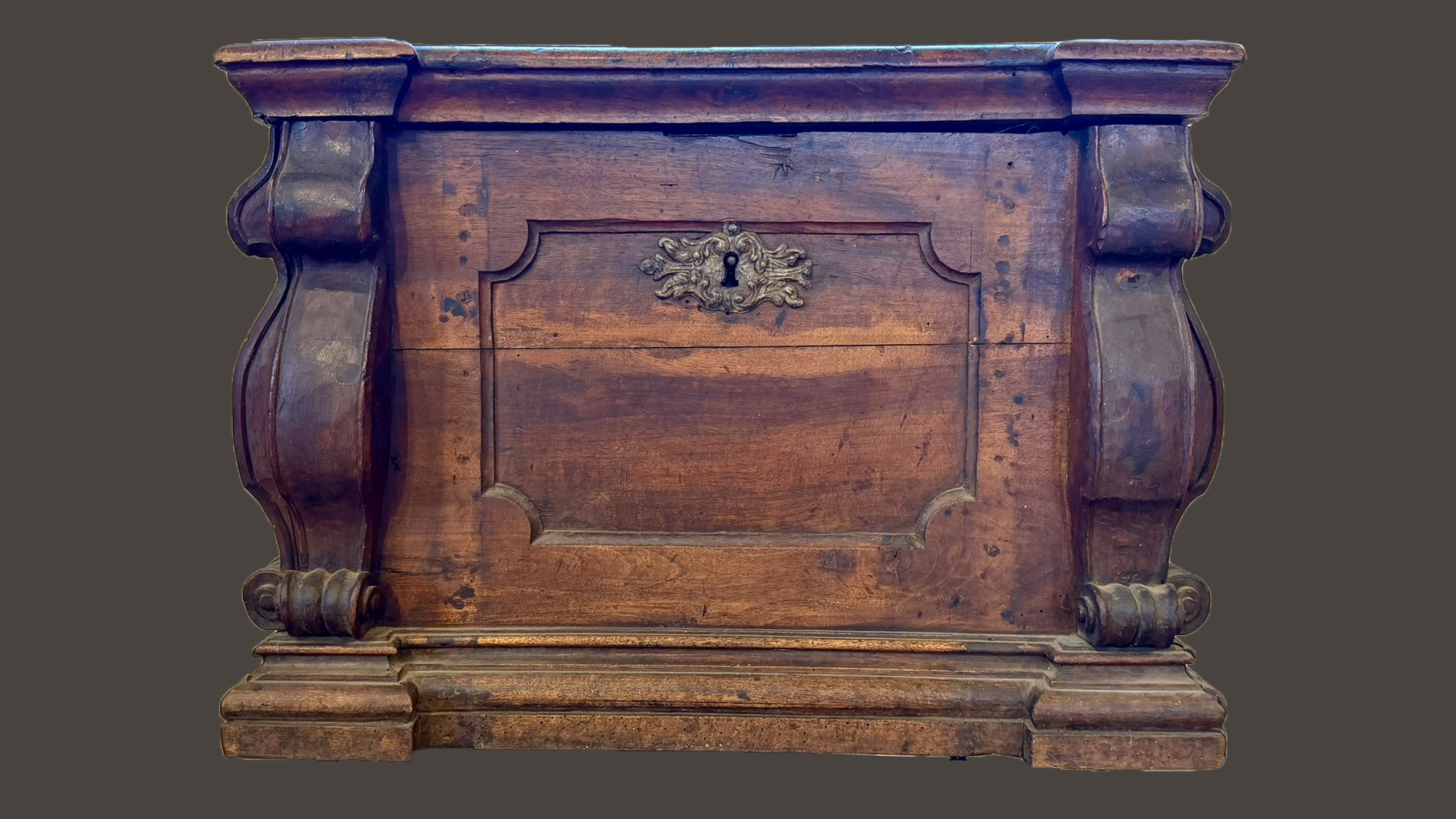 18th-century Baroque wooden chest with carved scroll consoles, panelled sides, and ornamental keyhole cartouche. Frontal view.